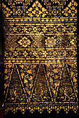 Wat Xieng Thong temple in Luang Prabang, Laos. Detail of the  intricate gold stencilling on black lacquer that decorate the walls of the sim. Floral motif. 